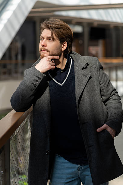 istock Stylish man in a coat and sweater poses thoughtfully in urban setting 2210583450