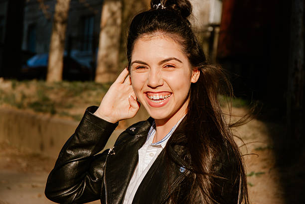 Joyful young woman smiling outdoors in sunlit urban setting.