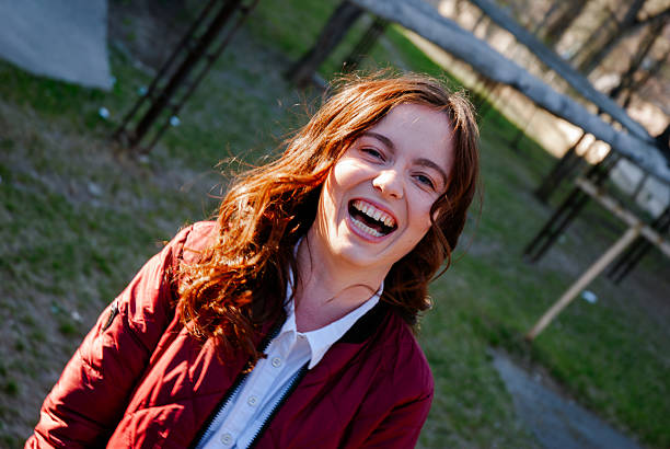 Joyful young woman laughing outdoors in a park setting.