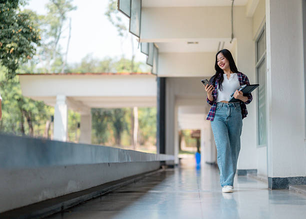 istock Young Asian student walking in university corridor using smartphone 2210591011