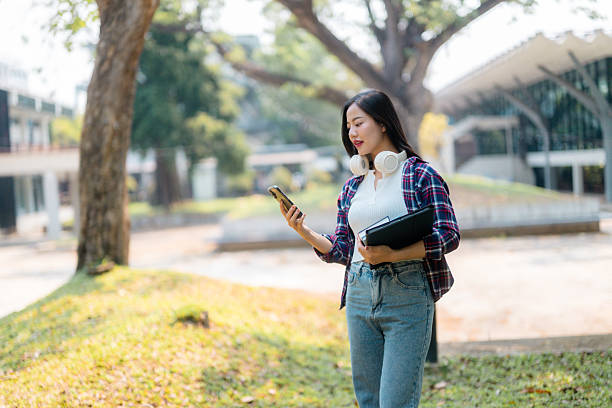istock Young Asian student walking in university park using smartphone 2210591058