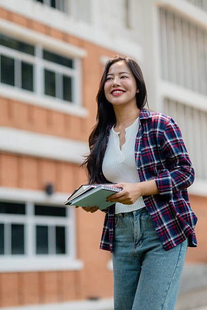 istock Smiling student walking and holding books in university campus 2210591555