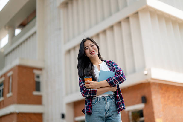 istock Smiling student holding books and coffee outside university building 2210591864