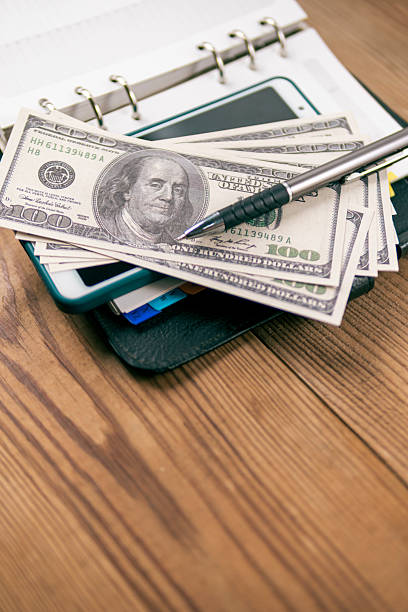 istock Hundred-dollar bills and a pen lay on an open planner. 2210592936