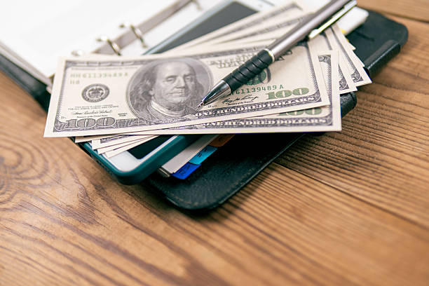 istock Hundred-dollar bills and a pen lay on an open planner. 2210592941