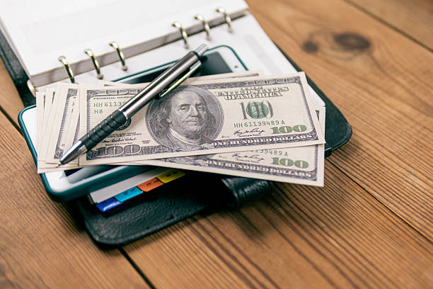 istock Hundred-dollar bills and a pen lay on an open planner. 2210592956