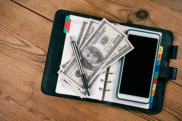 istock Hundred-dollar bills and a pen lay on an open planner. 2210592983