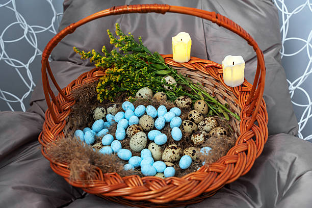 Top view of an Easter wicker basket with quail eggs, lighted candles and decorative blue eggs lying on the seat of a wicker swing.