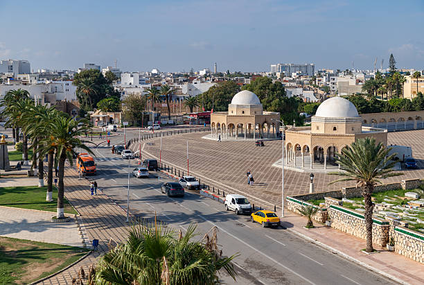 A scenic view of a Tunisian rooftop featuring intricate tile work and historic architecture. The sky is partly cloudy, adding depth to the vibrant setting. The scene captures the cultural essence of Tunis.