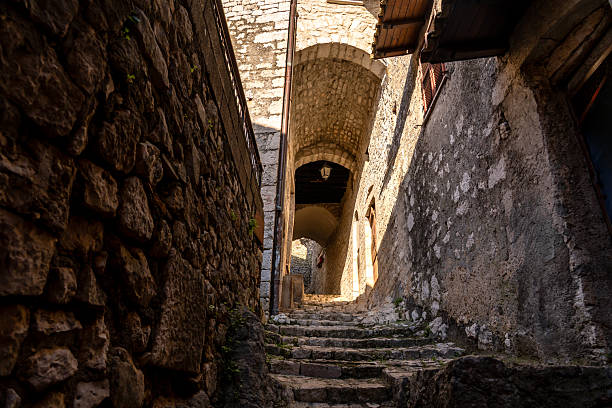 view from ground level upwards of a stone staircase of an alleyway passing under an archway and through stone walls affected by a strong contrast between light and shadow
