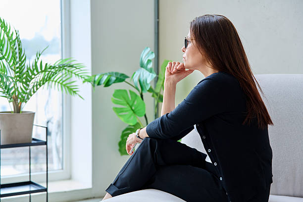 istock Serious anxious middle aged woman looking out window sitting on sofa 2210600632