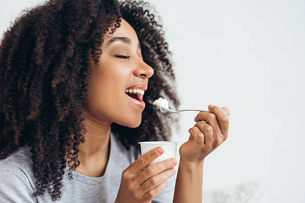 istock Happy young woman eating yogurt with spoon from plastic cup 2210604756