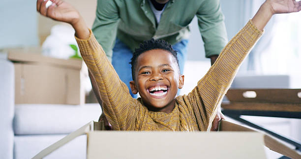 istock Black child, portrait and boxes game with dad in new home, relocation fun and playing support. Son, father and pushing kid in cardboard for fantasy race in living room, happy energy and moving house 2210607275