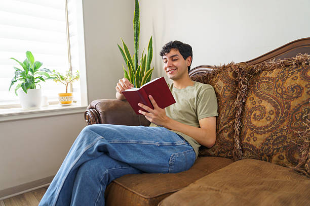 istock Young man relaxing on sofa reading a book at home 2210615139