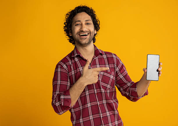 istock Happy man showing smart phone on yellow background 2210615764