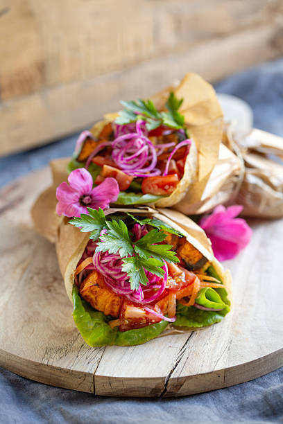 Two vibrant vegan wraps filled with vegetables, pickled onions, and flowers.