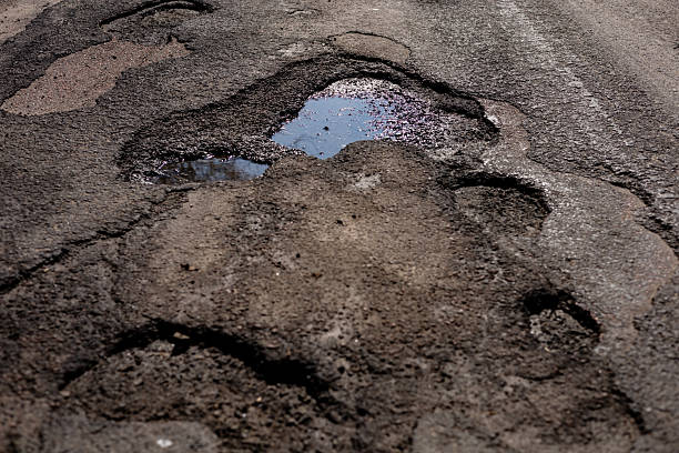 istock Large holes and cracks on the asphalt road indicate severe damage, posing risks to vehicles and requiring urgent repair efforts 2210628301