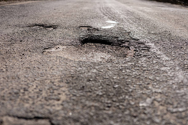 istock Significant damage to asphalt highway includes a large hole and cracks, requiring urgent repair to ensure safety for drivers 2210628304