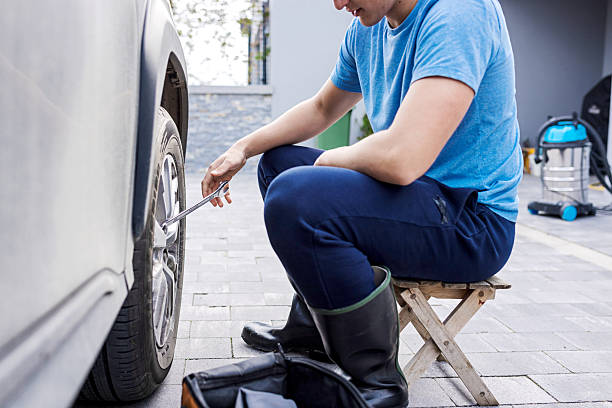 istock Man Repairing a Vehicle Tire Using a Wrench on a Driveway 2210628871