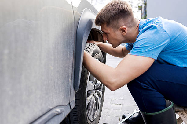 istock Man Inspecting Car Wheel for Maintenance Outdoors in a Driveway Setting 2210628875