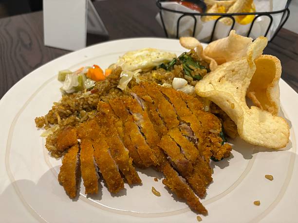 Indonesian fried rice with crispy chicken cutlet, served with egg, pickles, and crackers on a white ceramic plate.