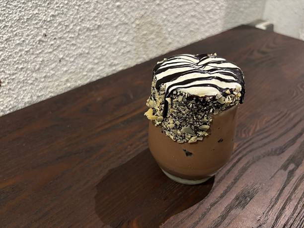 istock Decadent chocolate milkshake topped with whipped cream and chocolate drizzle, served in a nut-coated glass on a rustic wooden table 2210644012