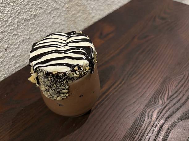 Decadent chocolate milkshake topped with whipped cream and chocolate drizzle, served in a nut-coated glass on a rustic wooden table
