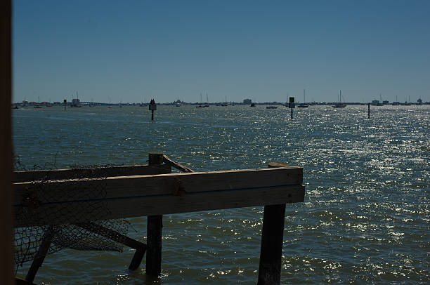 Serene Coastal Scene With a broken Dock and Sailboats on a Sunny Day. View out to Boca Ciega Bay in Gulfport, FL. Calm water under a clear blue sky with a wooden dock in the foreground, and a distance filled with sailboats and coastal scenery, evoking tranquility and relaxation. gulfport florida photos stock pictures, royalty-free photos & images