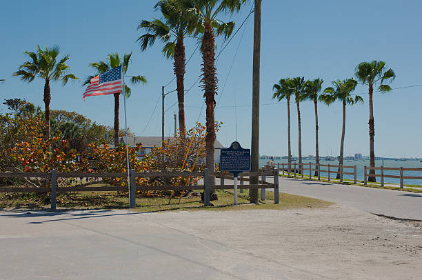 American Flag and Scenic Waterfront with Palms Under Clear Blue Sky American Flag and Scenic Waterfront with Palms Under Clear Blue Sky. Wide view towards Boca Ciega Bay from Clam Bayou Nature Preserve Gulfport, Florida. Leading line out to water. Blend of patriotism and tropical tranquility. gulfport florida photos stock pictures, royalty-free photos & images