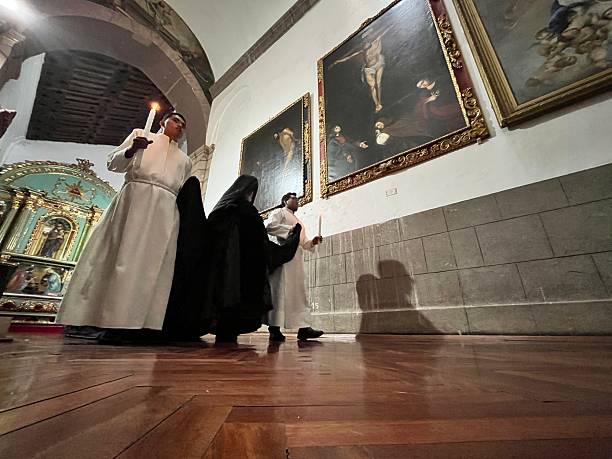 Quito, Pichincha, Ecuador - April 16, 2025: Cucuruchos, dressed in long black robes and hoods, carrying candles during the Arrastre de Caudas procession at the Metropolitan Cathedral in Quito, Ecuador, for Holy Week.The 