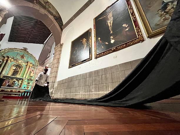 Quito, Pichincha, Ecuador - April 16, 2025: Cucuruchos, dressed in long black robes and hoods, carrying candles during the Arrastre de Caudas procession at the Metropolitan Cathedral in Quito, Ecuador, for Holy Week.The 