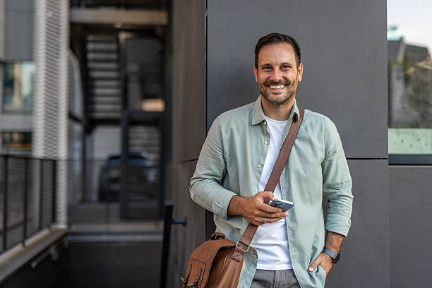 istock Smiling businessman using smartphone leaning against wall outside office 2210651642
