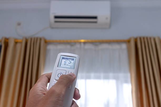 istock Hand holding AC remote control directed on the air conditioner to adjust temperature 2210655589