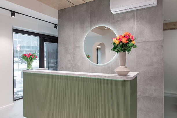 Contemporary office lobby featuring a green reception desk adorned with fresh floral arrangements. Reflective mirror decor and natural light enhance the clean and welcoming atmosphere.