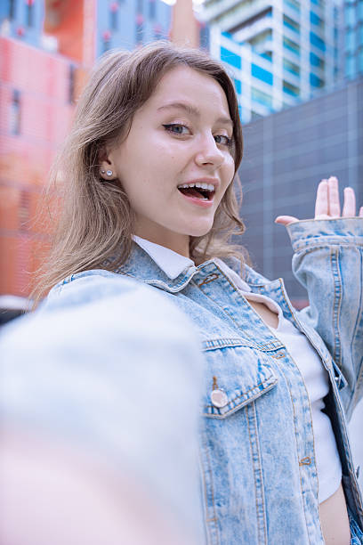 istock Caucasian young woman smiling and waving while taking selfie in urban setting 2210659347