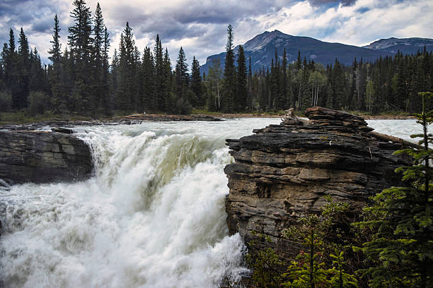 istock Cascading waterfall rushes over rocky ledge in a serene forest landscape surrounded by mountains during cloudy afternoon 2210661732
