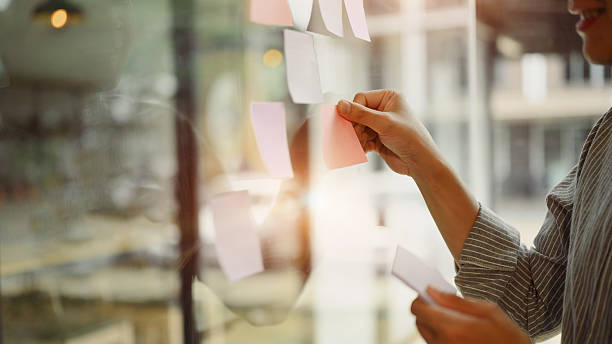istock Businessman placing colorful paper notes on transparent board during team strategy session. 2210664869
