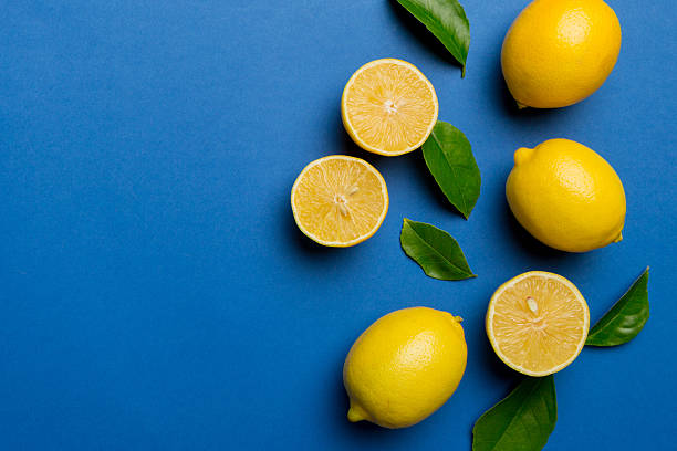 istock Many fresh ripe lemons with green leaves on colored background, top view, space for text 2210665333