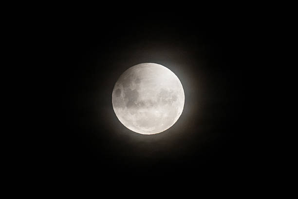 istock A photo of the moon during a partial eclipse, with its top edge slightly darkened and a soft haze from thin clouds diffusing the light 2210668235