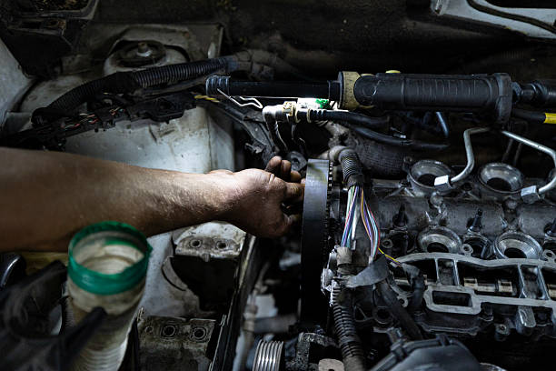 istock A mechanic's hand works on the timing belt area of a partially disassembled engine inside a vehicle, illuminated by a work light. 2210668436
