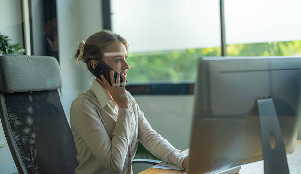 istock Professional woman engaged in a phone conversation while working at her desk in a modern office setting during daylight 2210674310