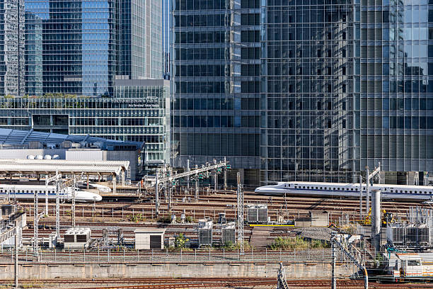 Tokyo, Japan - November 04, 2024: High-speed trains operate simultaneously at Tokyo Station, one arriving and the other departing, amid a complex rail infrastructure with power lines and towering business district buildings