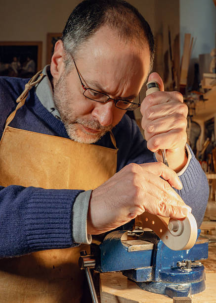 istock Caucasian luthier crafting violin scroll using gouge and vise in workshop 2210679147