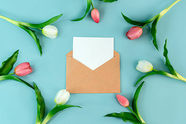 istock An envelope with a white blank sheet for writing on a blue background surrounded by spring tulips, a place for text 2210679380