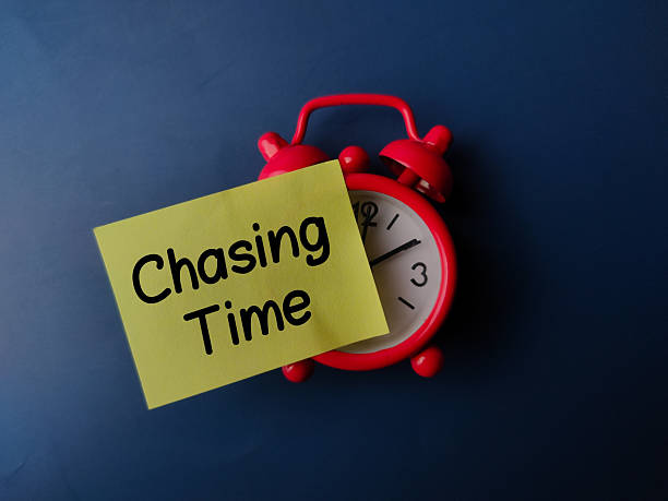 istock Alarm clock and sticky note with the word Chasing Time on blue background 2210680182