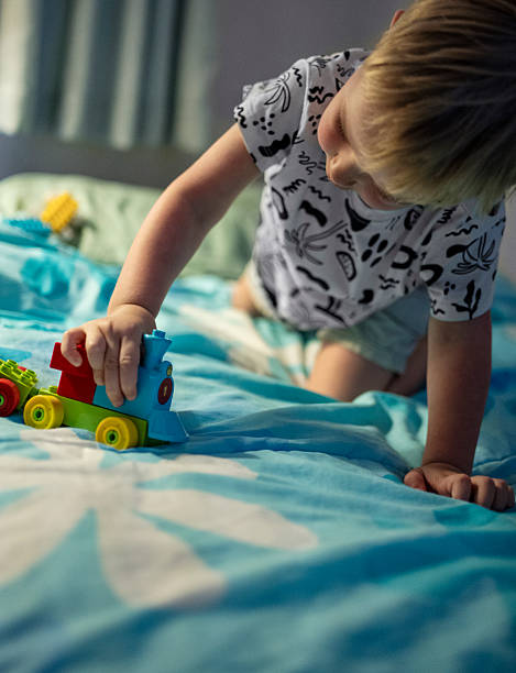 Little boy enjoying playing with colorful toy train on bed at home