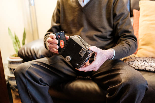 Senior man sitting on a sofa, holding a vintage camera and inserting the film, remembering old times