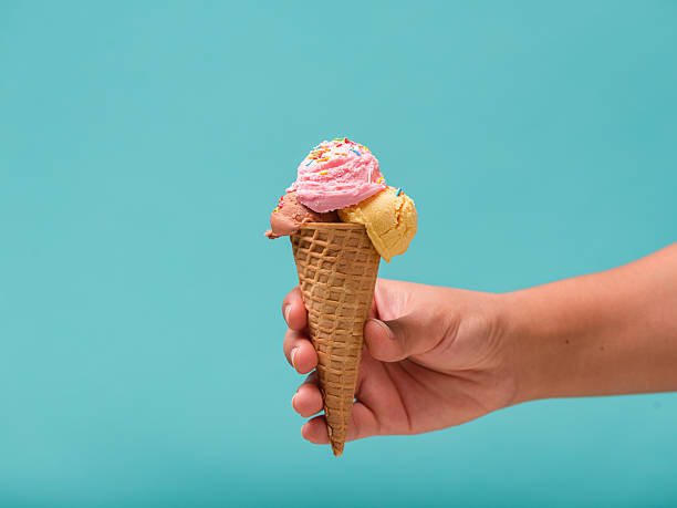 istock A hand holds a waffle cone overflowing with three scoops of ice cream adorned with colorful sprinkles. 2210683667