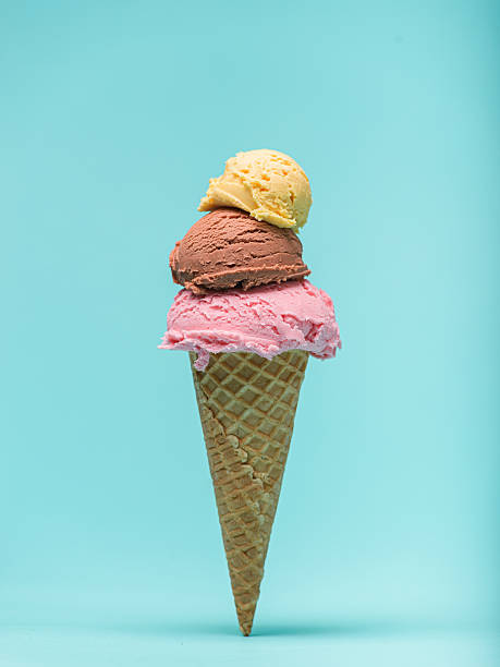 A waffle cone overflows with three scoops of ice cream: strawberry, chocolate, and vanilla. Blue background stock photo
