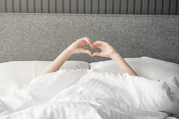 istock Hands forming heart shape above blanket in cozy bed setting with gray headboard. 2210684313